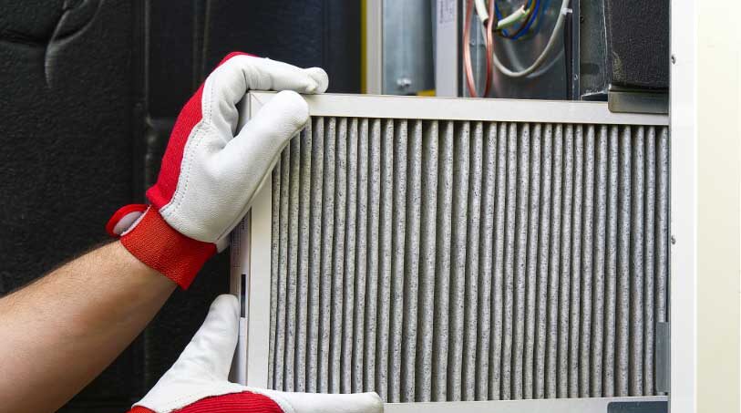 A person wearing gloves while replacing a clean air filter in a home HVAC system to improve air quality.