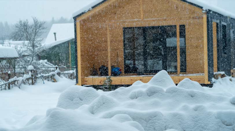 A wooden home covered in heavy snow during a winter storm, highlighting the importance of proper insulation in extreme weather conditions.