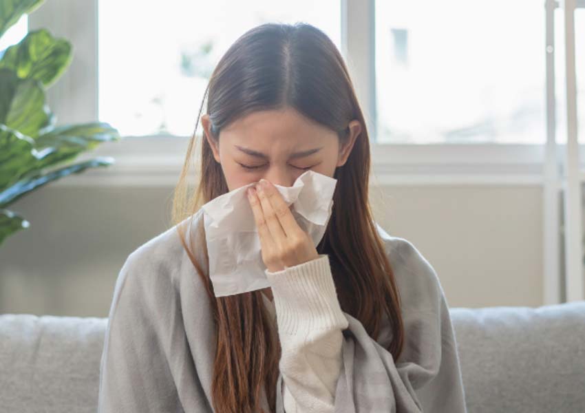 A woman wrapped in a blanket sneezing into a tissue, illustrating allergy symptoms that can be caused by mold.